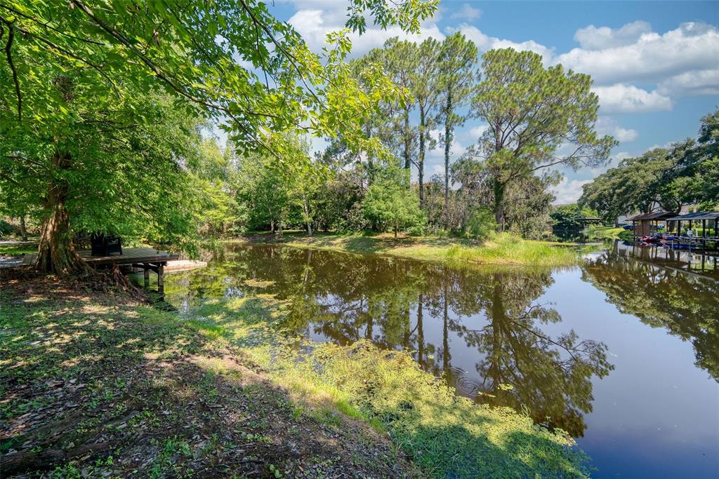 A wooden deck sits beside a calm, tree-lined pond under a partly cloudy blue sky — 12085 SANDY SHORES DRIVE UNIT D, WINDERMERE, FL