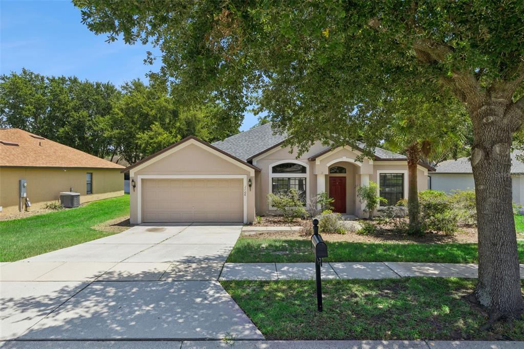 A single-story suburban house with a beige exterior, a two-car garage, and a red front door — 1106 NATURAL OAKS DRIVE, ORANGE CITY, FL