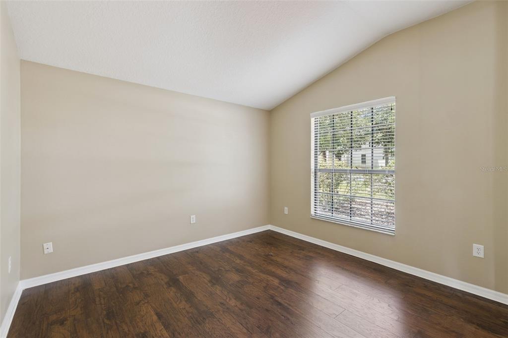An empty room with beige walls, dark wood flooring, and a single window with blinds — 1106 NATURAL OAKS DRIVE, ORANGE CITY, FL