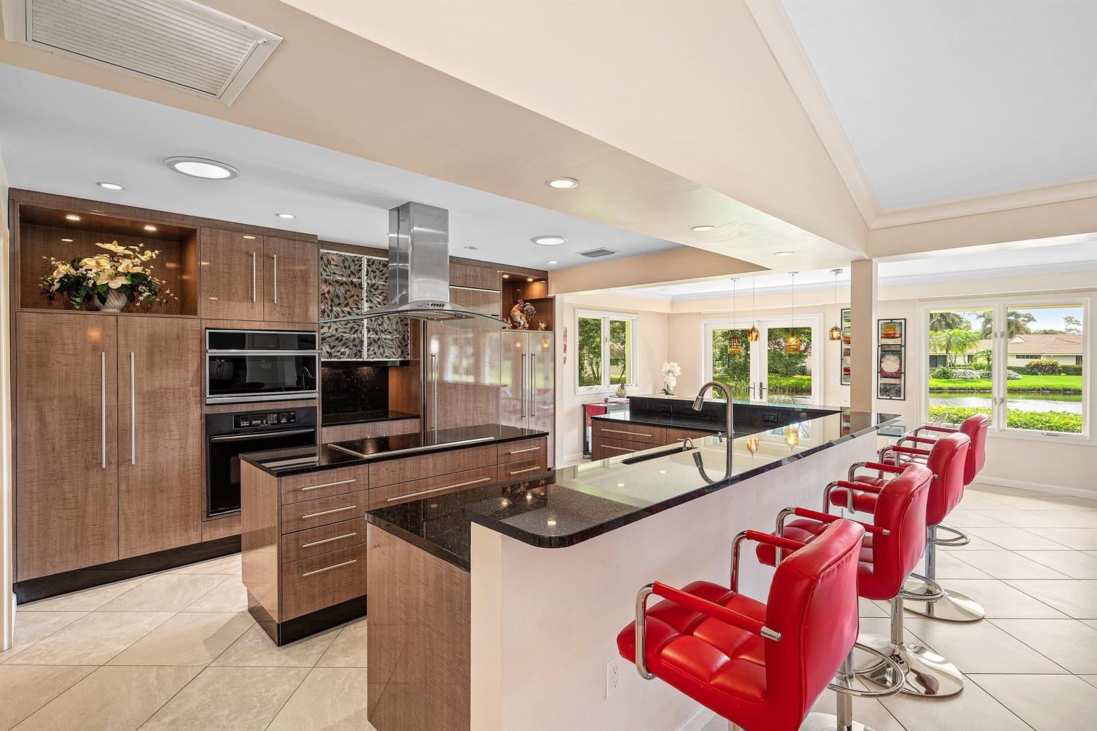 A modern kitchen features wood cabinets, black granite countertops, and four red bar stools — 4365 Shelldrake Lane, Boynton Beach FL 33436, BOYNTON BEACH, FL