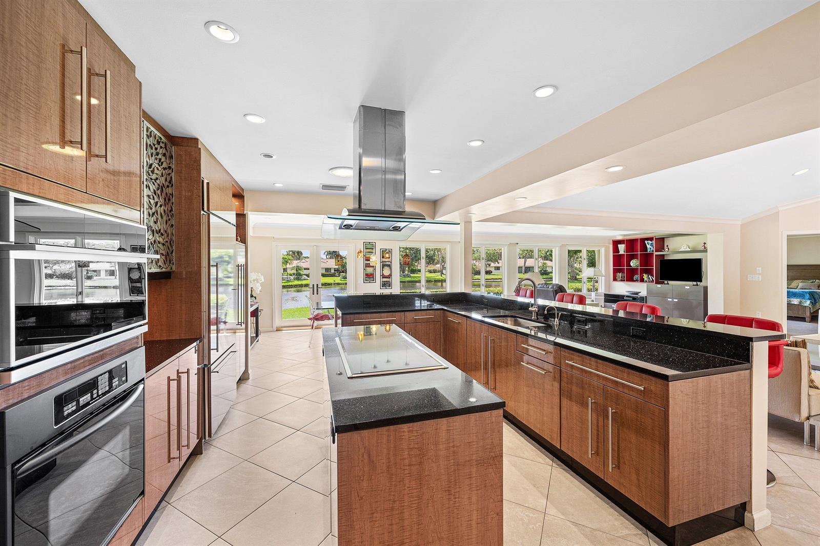 A modern kitchen features wood cabinets, black granite countertops, a central island, and lake views — 4365 Shelldrake Lane, Boynton Beach FL 33436, BOYNTON BEACH, FL