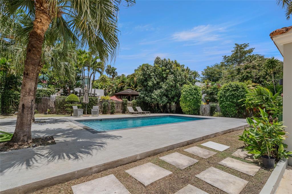 A rectangular swimming pool sits on a concrete patio surrounded by palm trees and landscaping — 30, G St., Villa Caparra G, GUAYNABO, PR