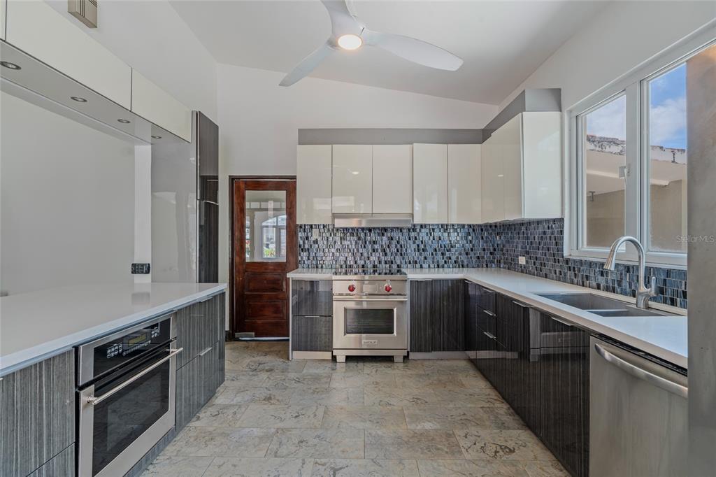 A modern kitchen features two-toned cabinetry, stainless steel appliances, a tiled backsplash, and stone flooring — 30, G St., Villa Caparra G, GUAYNABO, PR
