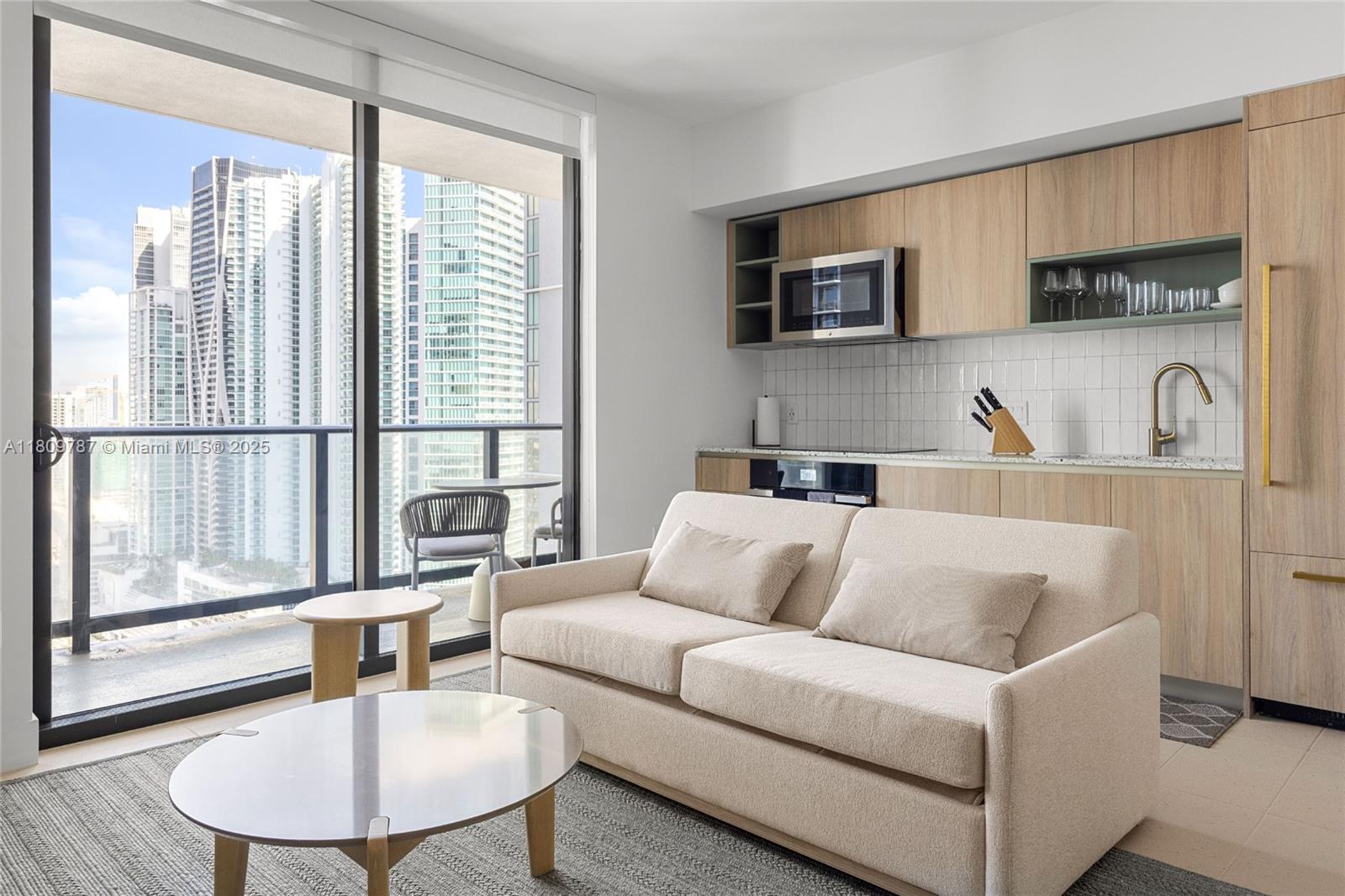 A modern studio apartment features a kitchenette, a beige sofa, and a balcony with city views — 159 NE 6th St # 2901, Miami FL 33132, MIAMI, FL