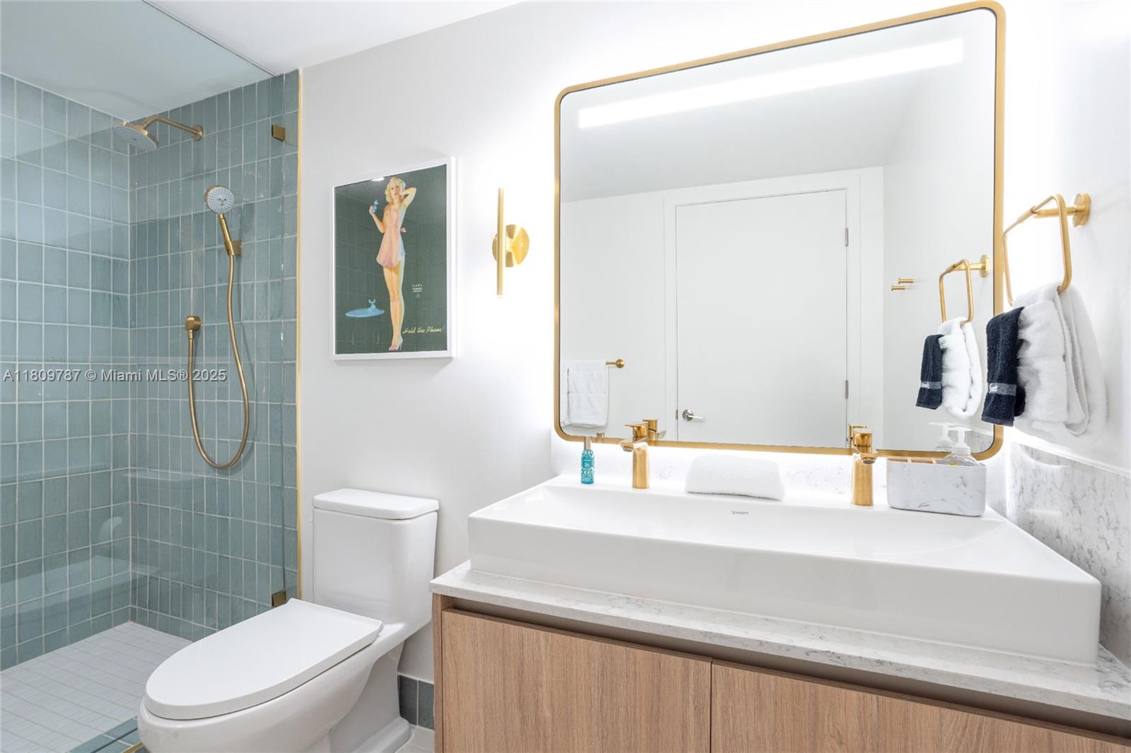 A modern bathroom features a glass-enclosed shower with blue tiles, a vanity, and gold fixtures — 159 NE 6th St # 2901, Miami FL 33132, MIAMI, FL