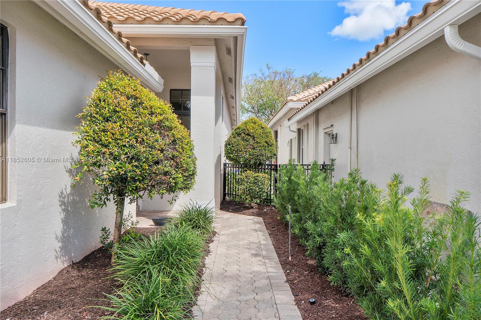 A paved walkway leads between two stucco houses with tiled roofs and landscaped garden beds — 2449 NW 64th St, Boca Raton FL 33496, BOCA RATON, FL