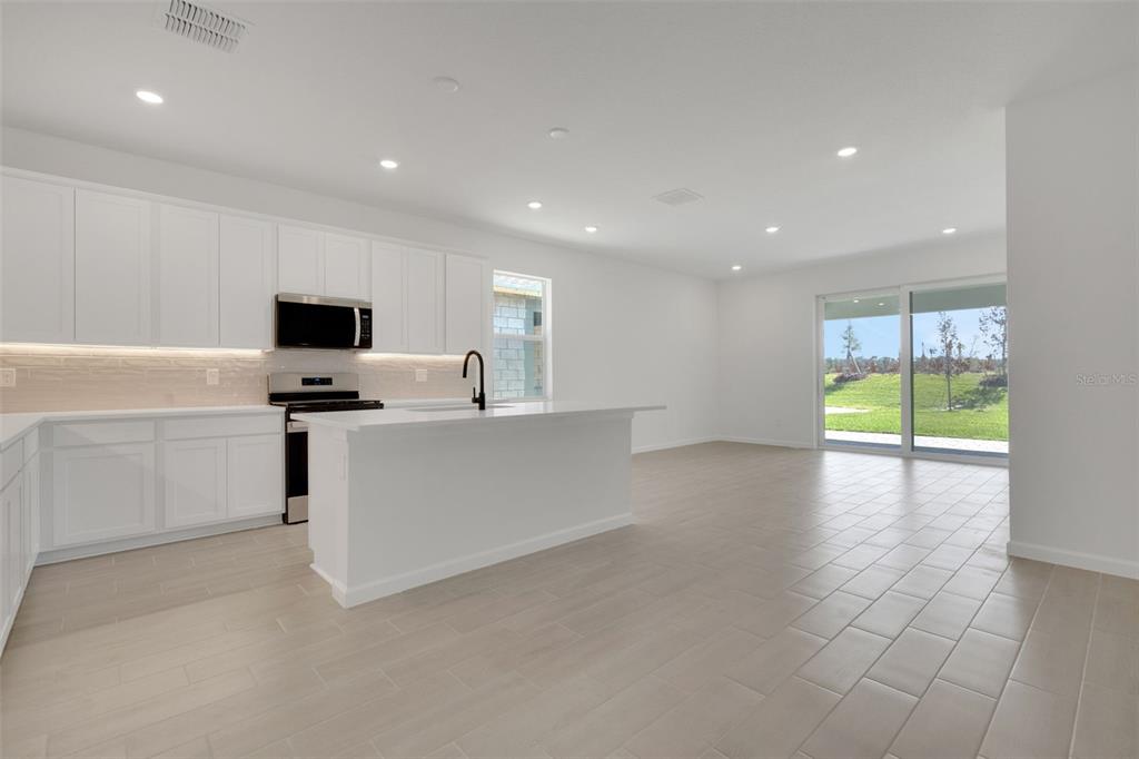 A bright kitchen features white cabinets, a central island, and tile flooring with sliding glass doors — 5436 NW CAMBERLY COURT, PORT ST LUCIE, FL