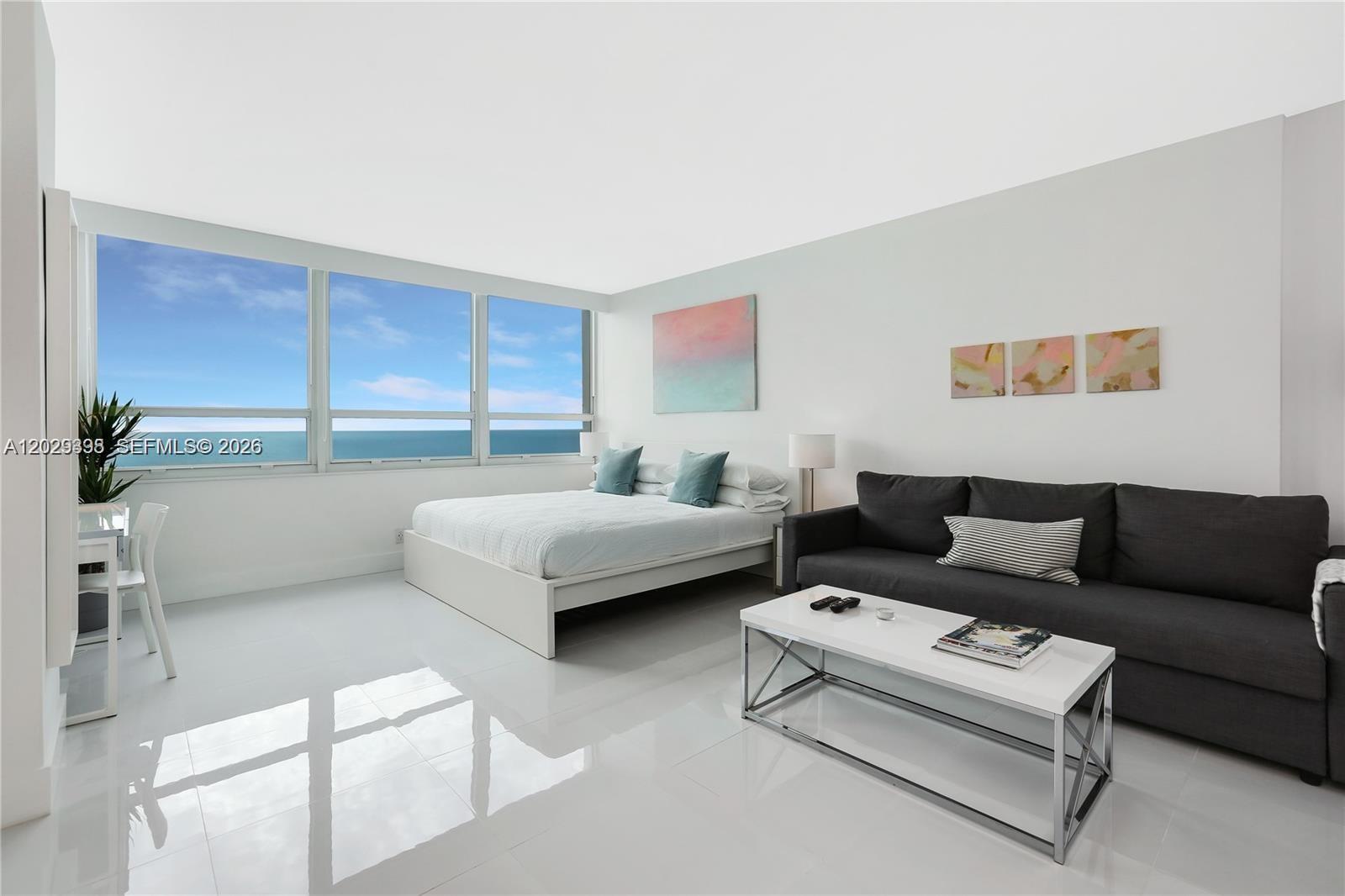 A bedroom with a bed, sofa, coffee table, and large windows overlooking the ocean — 5445 Collins Avenue, Miami Beach FL 33140, MIAMI BEACH, FL