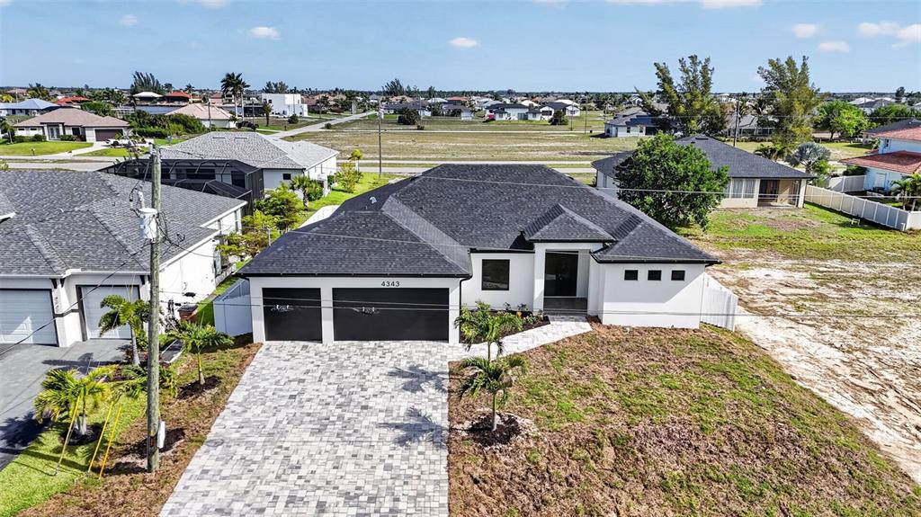 An aerial view shows a modern white house with a dark roof and paved driveway — 4343 NW 31ST TERRACE, CAPE CORAL, FL