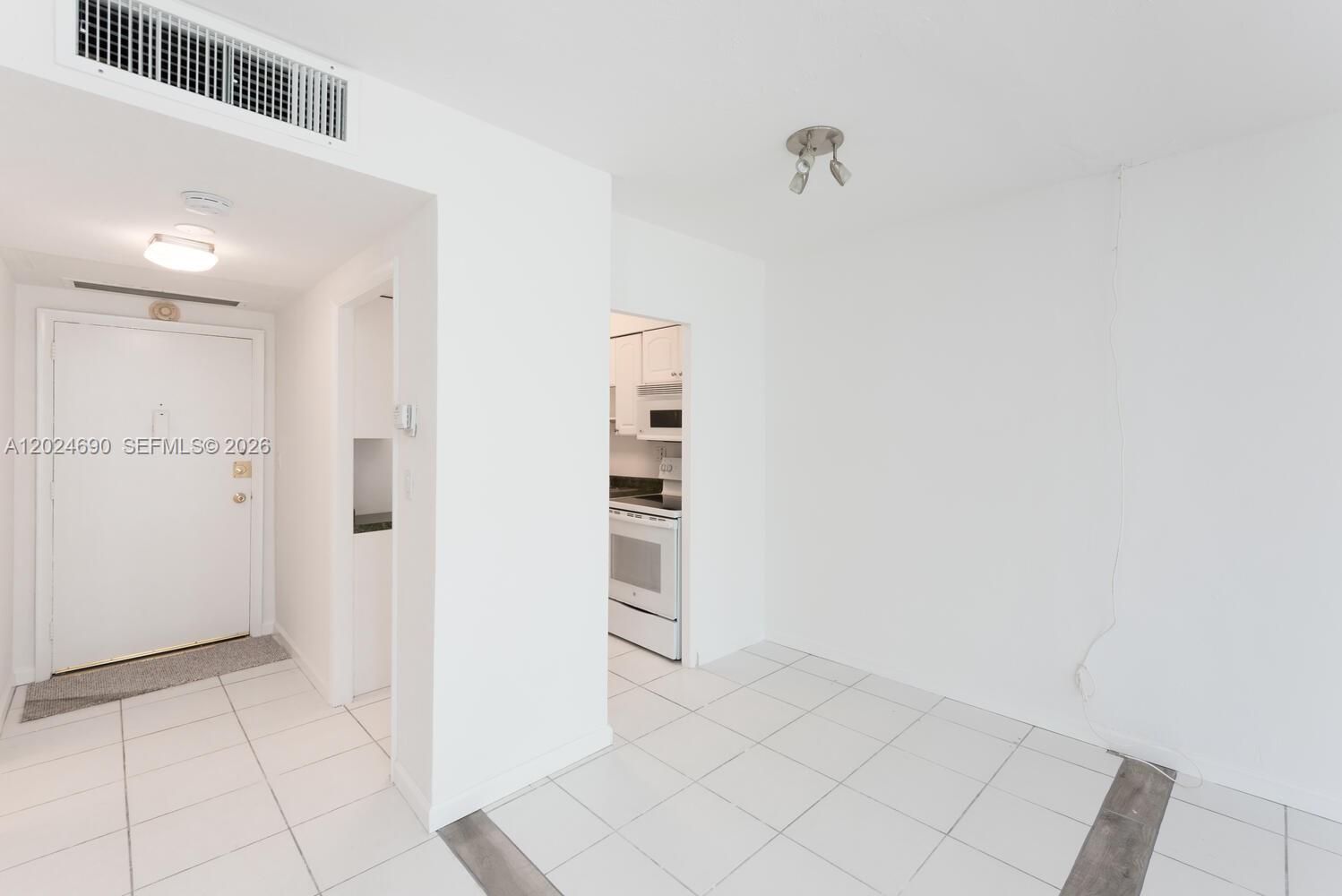 A bright, white-tiled living area features a large mirrored wall and an adjacent kitchen — 1408 Brickell Bay Dr # 1116, Miami FL 33131, MIAMI, FL