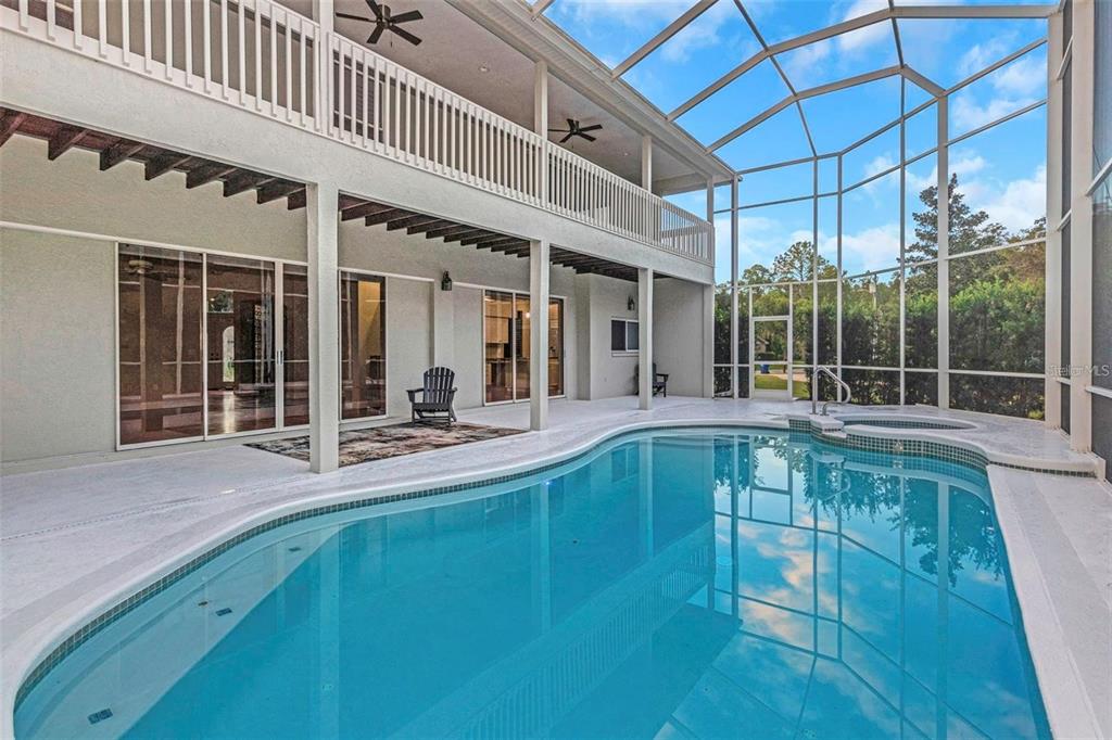 A two-story house exterior features a screened-in pool and patio area with ceiling fans — 5250 MACOSO COURT, NEW PORT RICHEY, FL