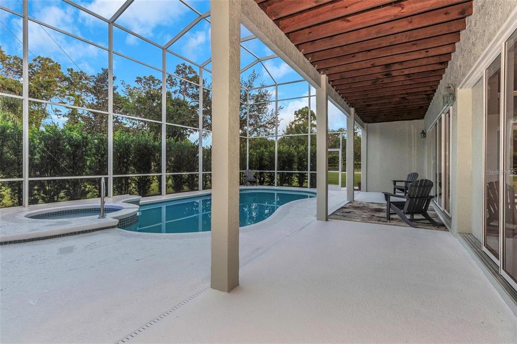 A screened-in patio features a swimming pool, a hot tub, and a wooden pergola ceiling — 5250 MACOSO COURT, NEW PORT RICHEY, FL