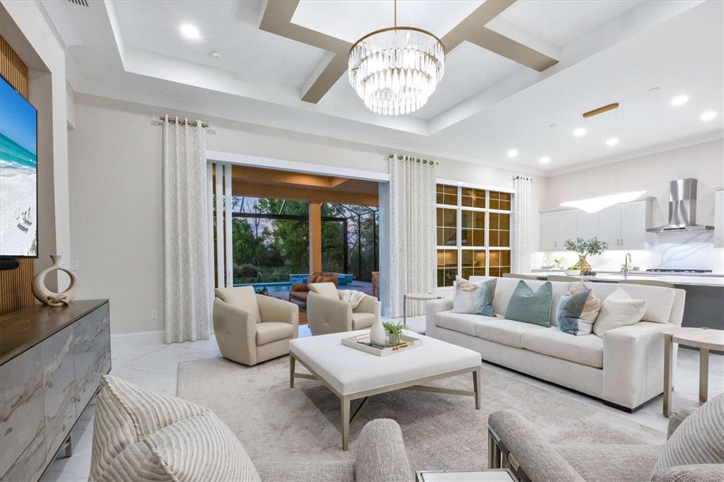 A bright living room features a coffered ceiling, chandelier, white sofa, and sliding glass doors — 8352 SEA GLASS COURT, SARASOTA, FL