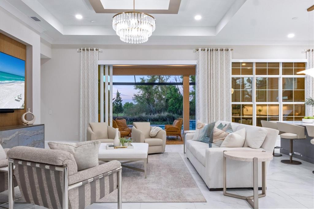 A modern living room features a large sectional sofa, two armchairs, and sliding glass doors — 8352 SEA GLASS COURT, SARASOTA, FL