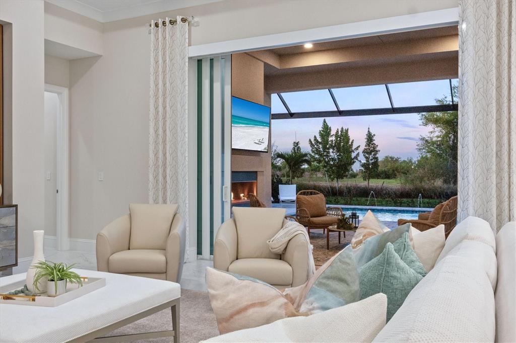 A living room with beige armchairs opens to a covered patio with a pool view — 8352 SEA GLASS COURT, SARASOTA, FL