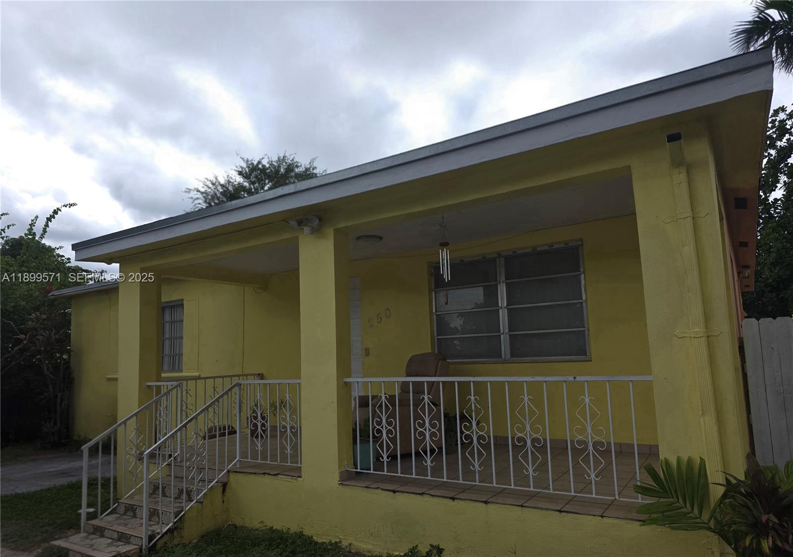 A yellow house features a covered front porch with white metal railings and stairs — 250 NW 63rd Ct, Miami FL 33126, MIAMI, FL