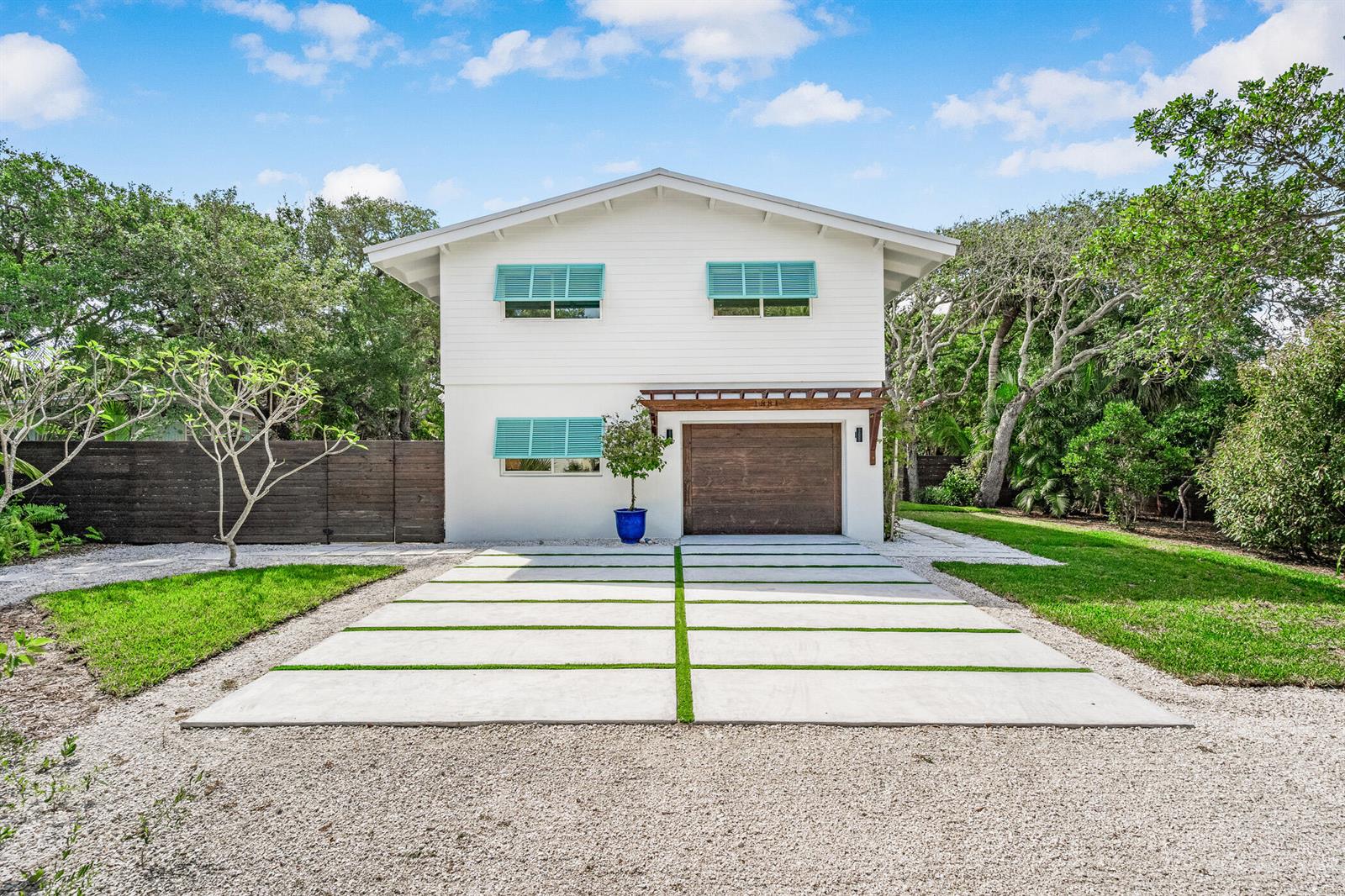 A two-story white house features a wooden garage door, turquoise shutters, and a concrete driveway — 1881 E Pebble Path, Vero Beach FL 32963, VERO BEACH, FL