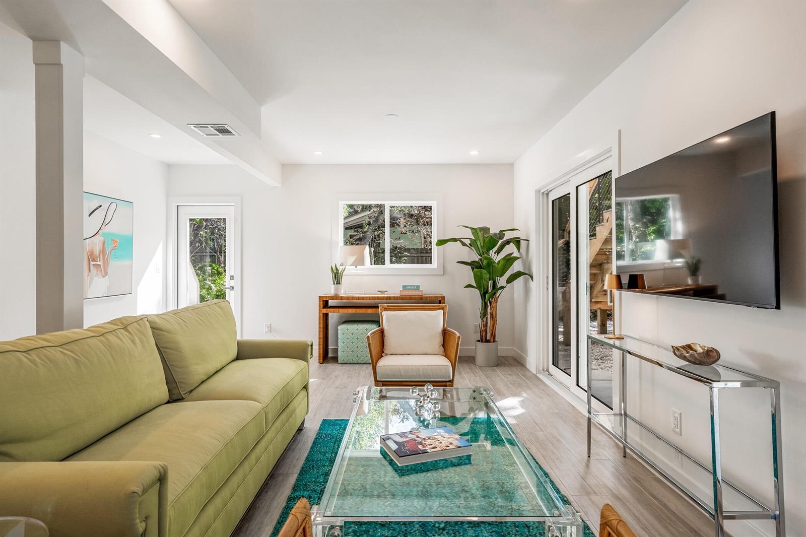 A living room features a green sofa, glass coffee table, armchair, and a wall-mounted television — 1881 E Pebble Path, Vero Beach FL 32963, VERO BEACH, FL