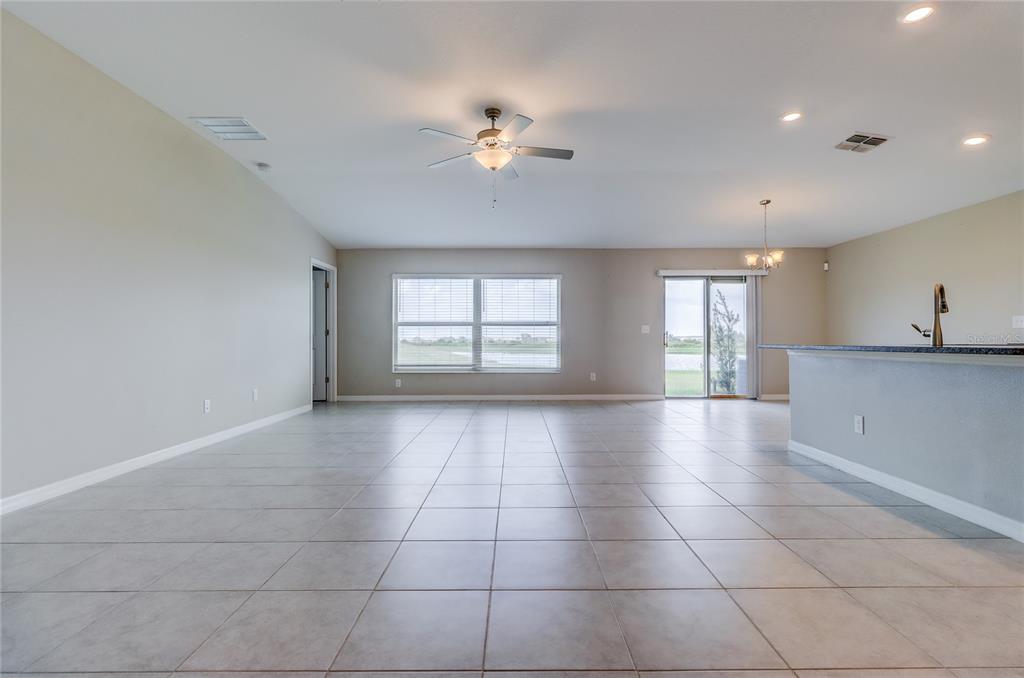 An open-concept living area features light tile flooring, a ceiling fan, and sliding glass doors — 8694 PARSONS HILL BOULEVARD, WESLEY CHAPEL, FL