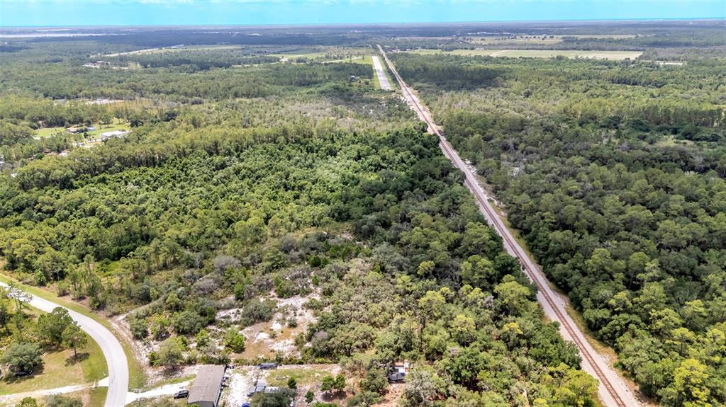 An aerial view shows a railroad track running through a dense, wooded landscape — WOODSTORK WAY, FROSTPROOF, FL