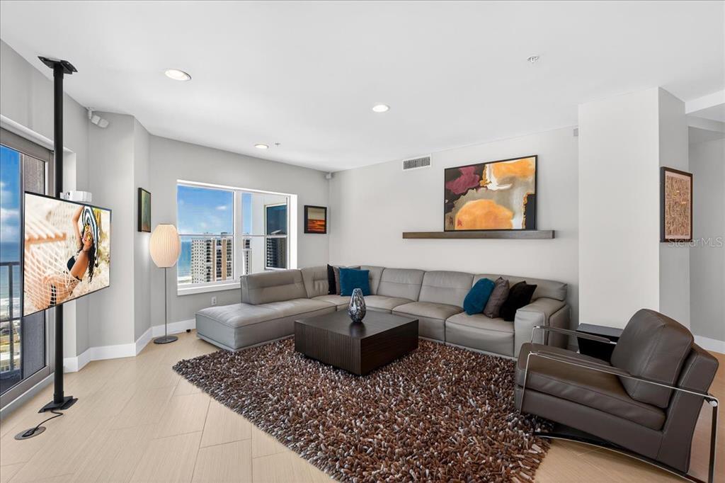 A living room features a grey sectional sofa, a brown rug, and a television on a stand — 2 OCEANS WEST BOULEVARD UNIT 2006, DAYTONA BEACH, FL