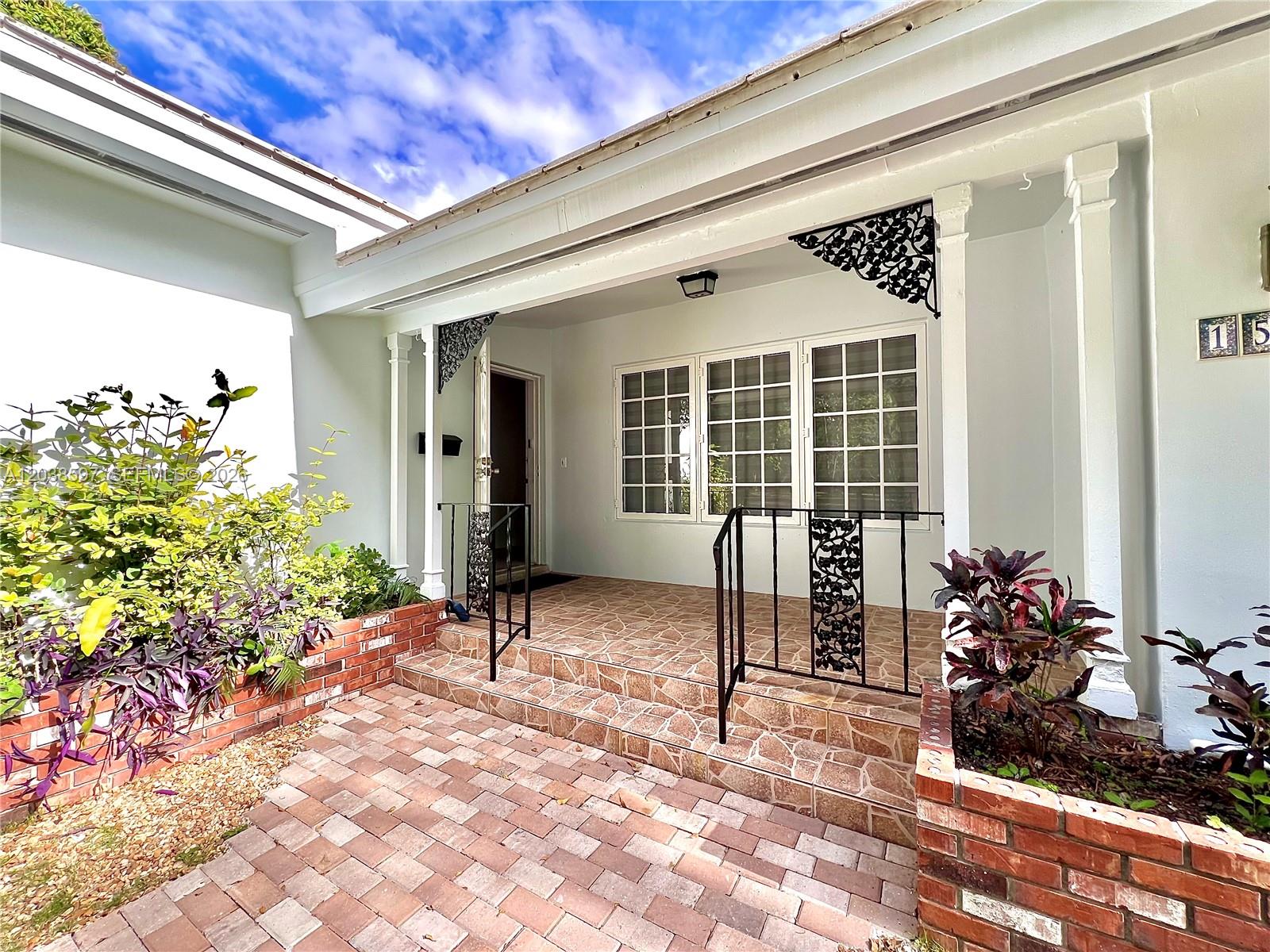 The exterior of a house features a brick-paved walkway, a tiled porch, and decorative iron railings — 1506 Delgado Ave, Coral Gables FL 33146, CORAL GABLES, FL