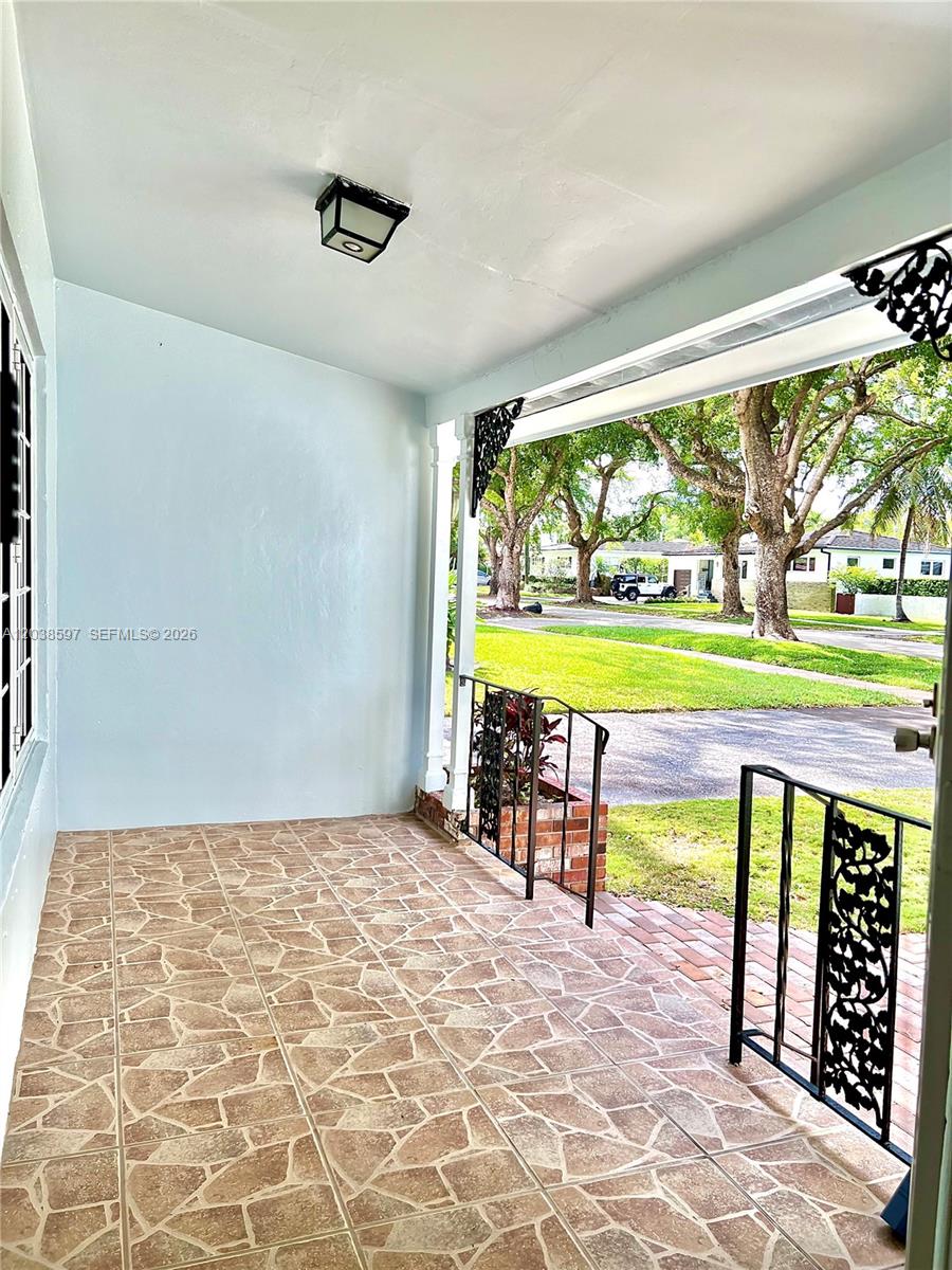 A covered front porch features light blue walls, a tiled floor, and black metal railings — 1506 Delgado Ave, Coral Gables FL 33146, CORAL GABLES, FL