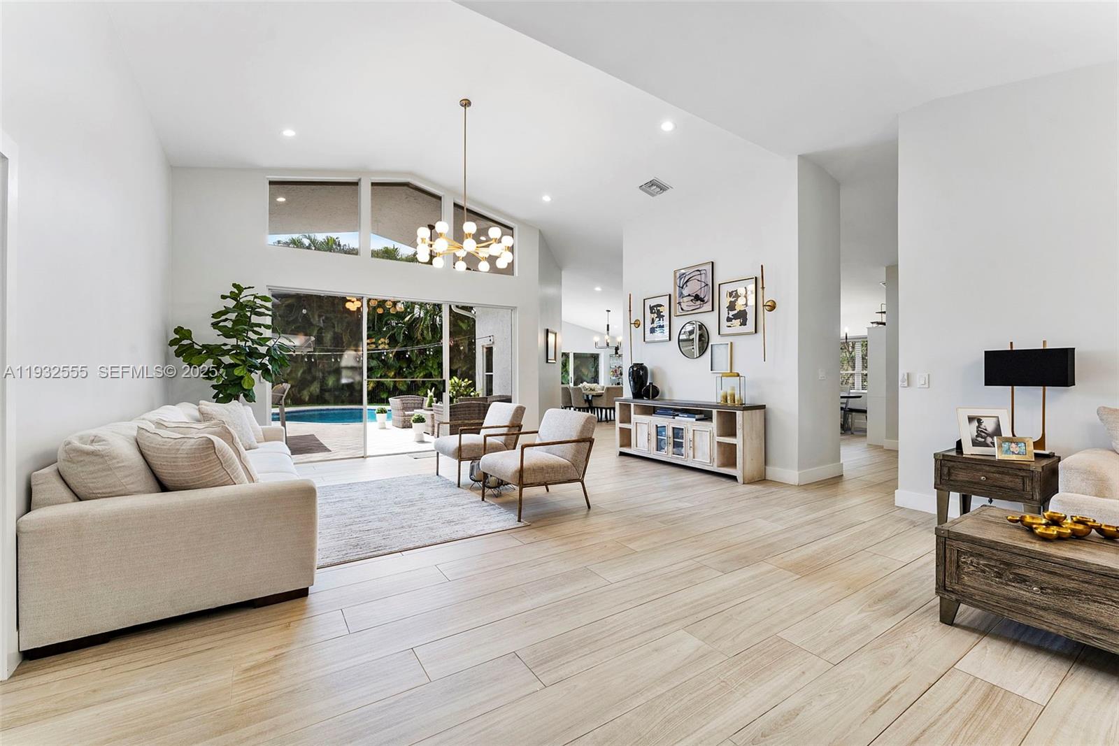 A bright living room features light wood-look tile floors, vaulted ceilings, and a pool view — 550 NW 110th Ave, Plantation FL 33324, PLANTATION, FL