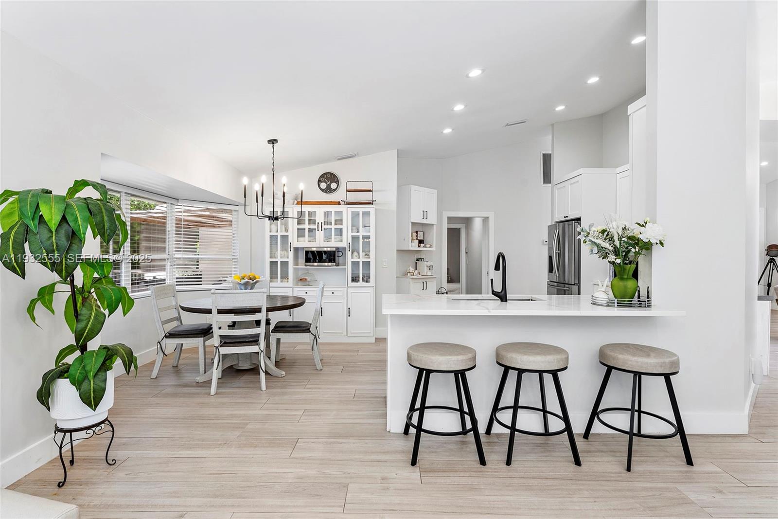 A bright, open-concept kitchen and dining area features white cabinetry, a breakfast bar, and stools — 550 NW 110th Ave, Plantation FL 33324, PLANTATION, FL