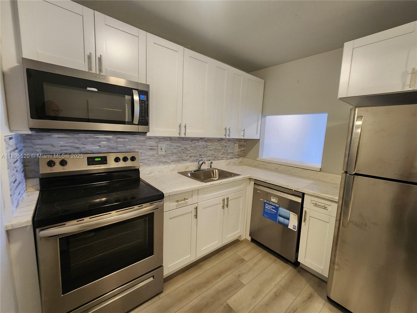 A kitchen features white cabinets, stainless steel appliances, a tiled backsplash, and light wood flooring — 11309 SW 200th St # C, Miami FL 33157, MIAMI, FL