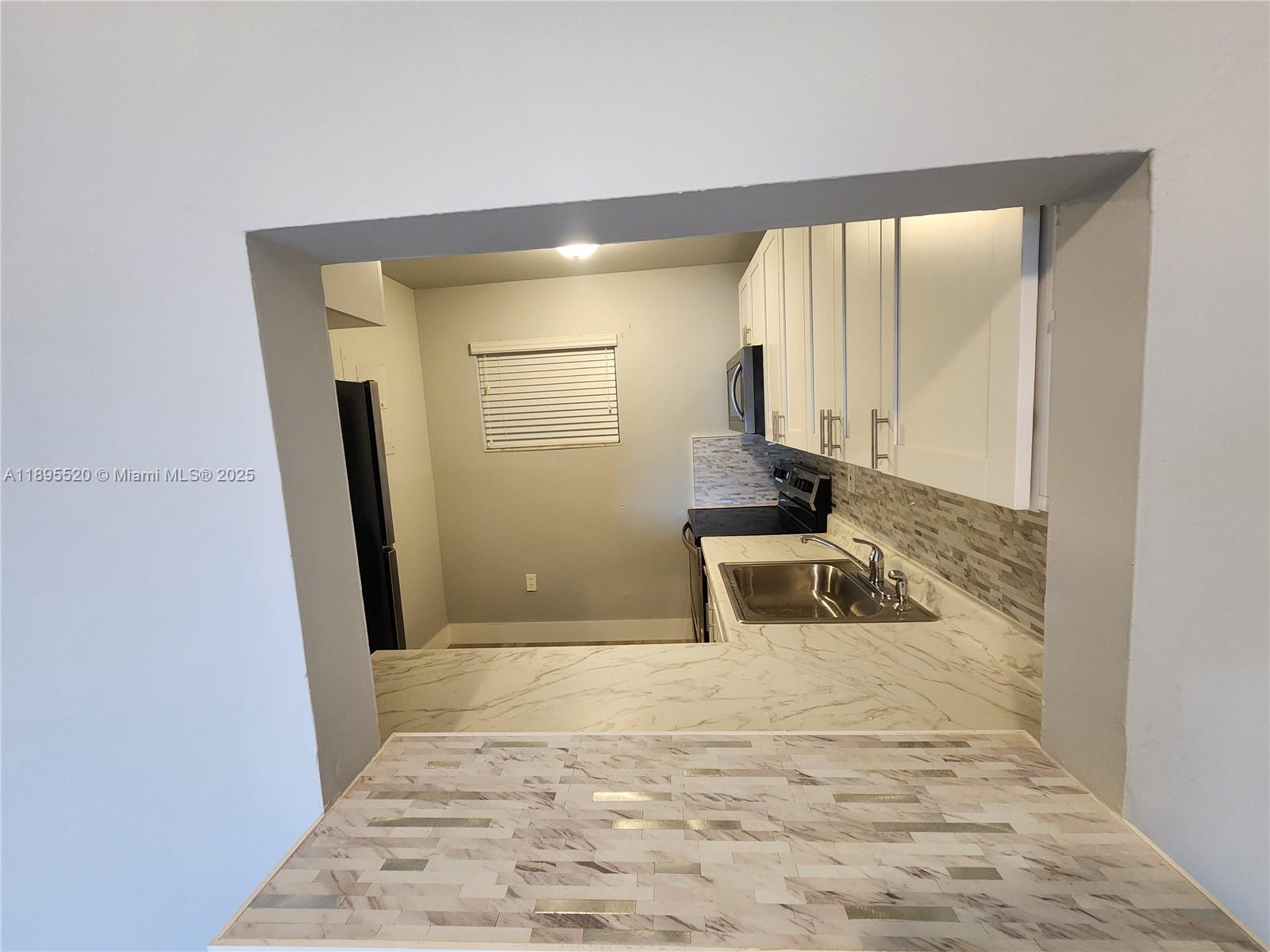 A kitchen features white cabinets, marble-patterned countertops, and a tiled backsplash viewed through a pass-through — 11309 SW 200th St # C, Miami FL 33157, MIAMI, FL