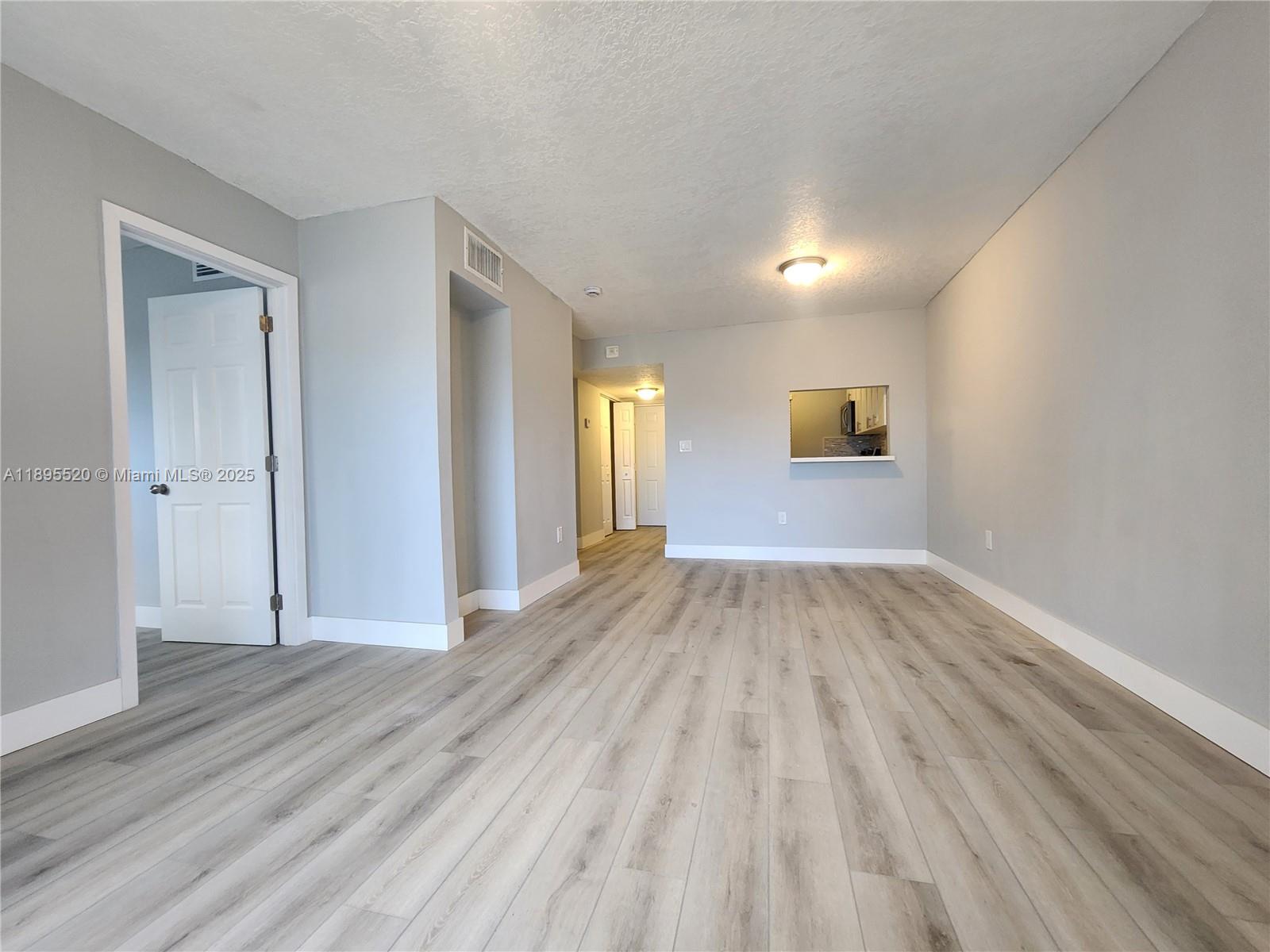 An empty living room features light gray walls, wood-look flooring, and a kitchen pass-through window — 11309 SW 200th St # C, Miami FL 33157, MIAMI, FL