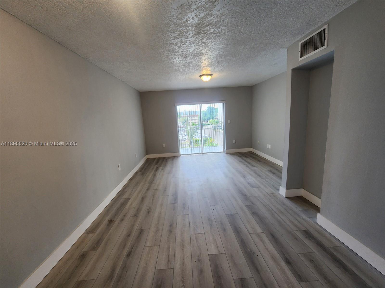 An empty living room features gray walls, wood-look flooring, and a sliding glass door — 11309 SW 200th St # C, Miami FL 33157, MIAMI, FL