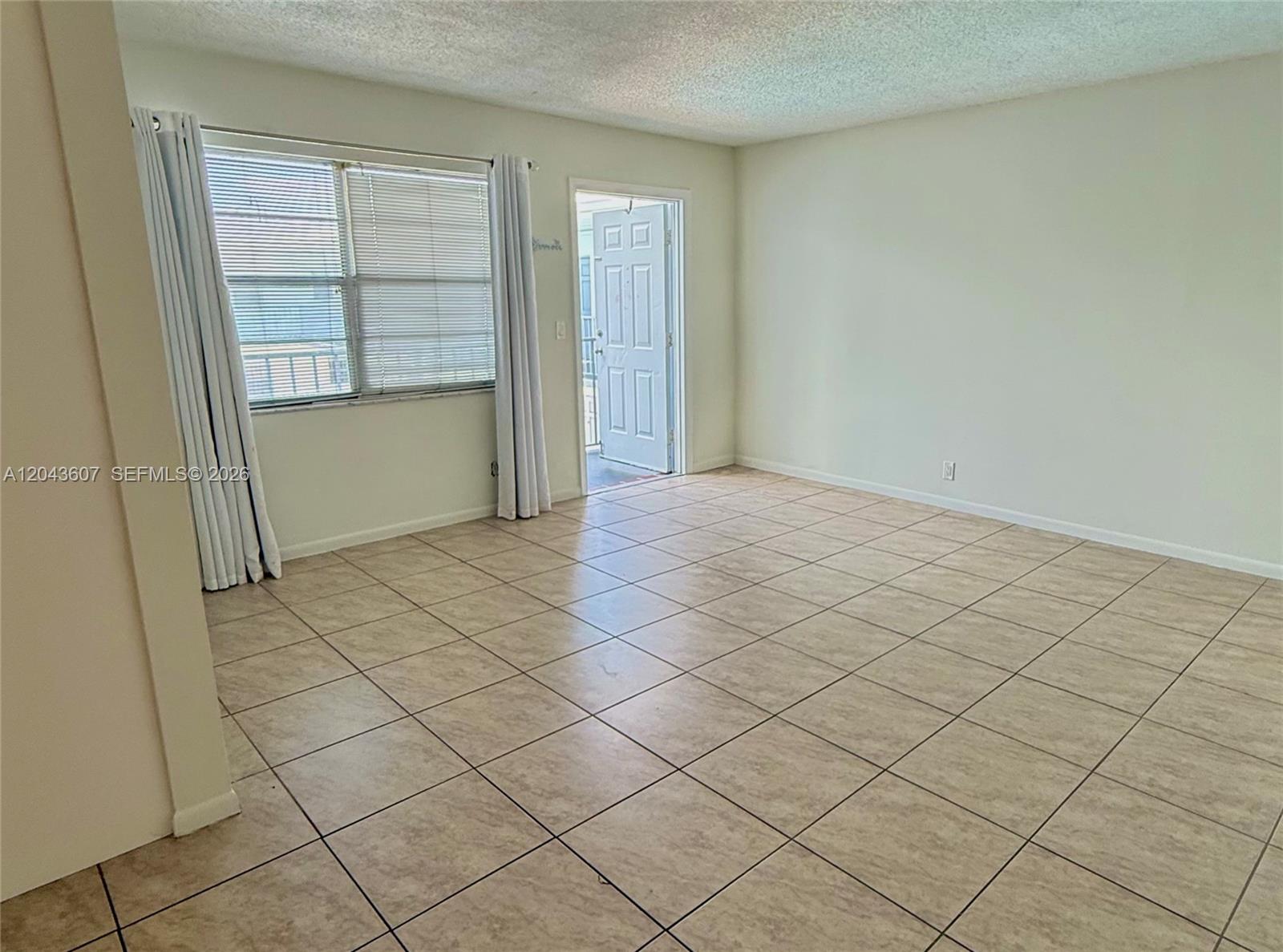 An empty room features beige tile flooring, white walls, and a door leading outside — 30 SE 4th Ave # 206, Hallandale Beach FL 33009, HALLANDALE BEACH, FL
