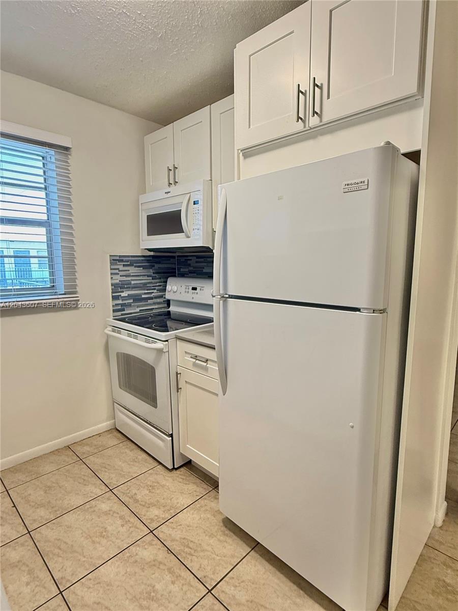A kitchen features white cabinetry, a white refrigerator, a white stove, and a blue backsplash — 30 SE 4th Ave # 206, Hallandale Beach FL 33009, HALLANDALE BEACH, FL