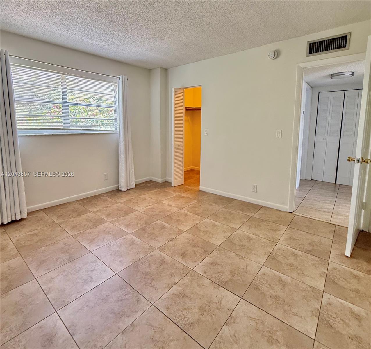 An empty bedroom features beige tile flooring, white walls, a window with blinds, and closets — 30 SE 4th Ave # 206, Hallandale Beach FL 33009, HALLANDALE BEACH, FL