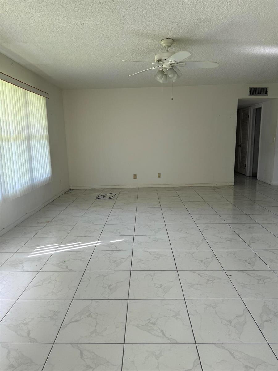 An empty room features white marble-patterned tile flooring, white walls, and a ceiling fan — 211 Country Lane # A, Boynton Beach FL 33435, BOYNTON BEACH, FL