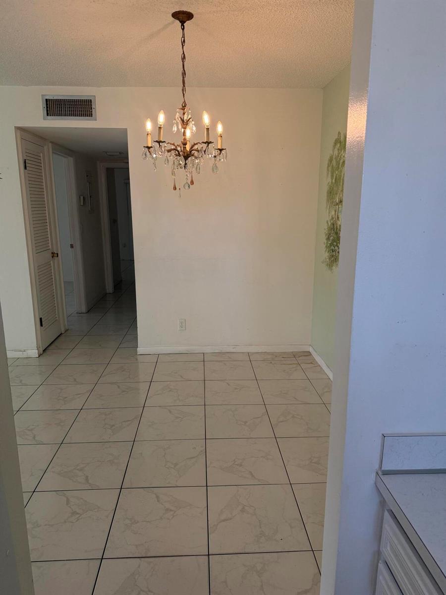 A dining area features a crystal chandelier, white walls, and light-colored tiled flooring — 211 Country Lane # A, Boynton Beach FL 33435, BOYNTON BEACH, FL