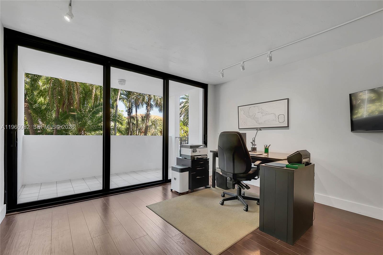 A home office features dark wood flooring, a desk, and sliding glass doors to a balcony — 100 Ocean Lane Dr # 202, Key Biscayne FL 33149, KEY BISCAYNE, FL