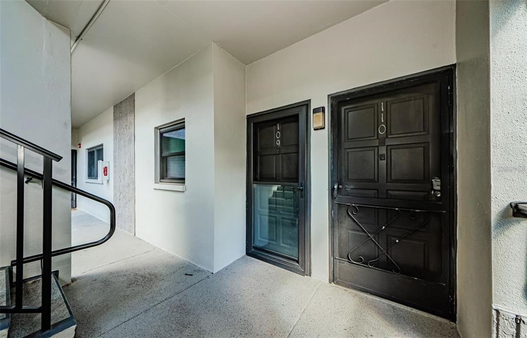 An exterior view of a building corridor featuring two dark doors labeled 109 and 110 — 2650 COUNTRYSIDE BOULEVARD UNIT F110, CLEARWATER, FL