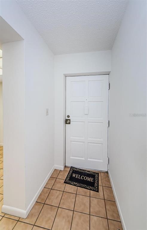 An entryway features a white door, a welcome mat, and light brown tiled flooring — 2650 COUNTRYSIDE BOULEVARD UNIT F110, CLEARWATER, FL