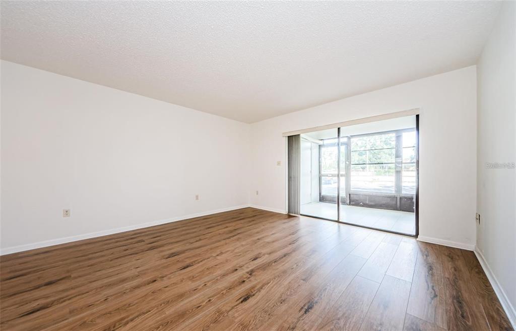 An empty room with wood-look flooring and a sliding glass door leading to a screened porch — 2650 COUNTRYSIDE BOULEVARD UNIT F110, CLEARWATER, FL