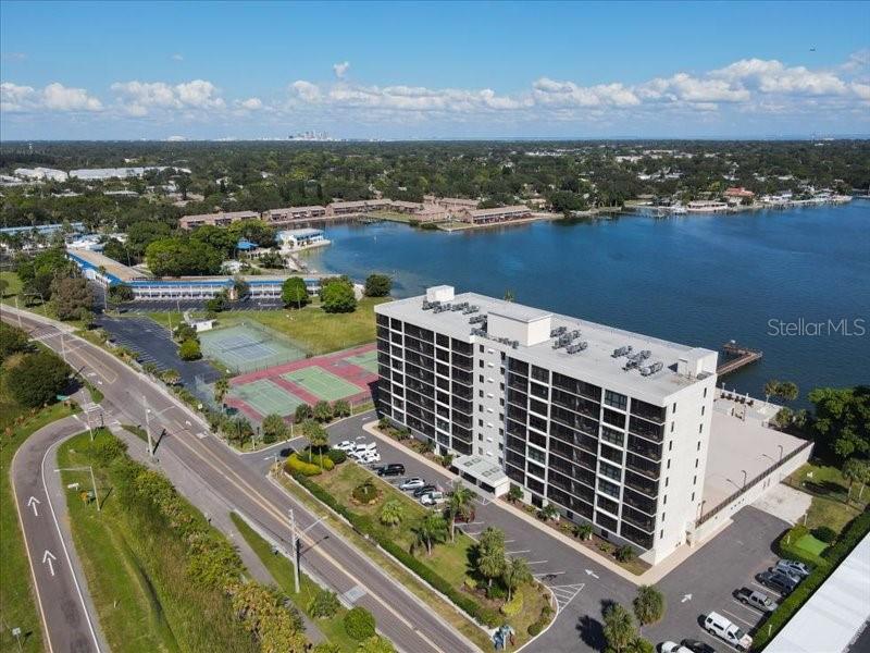 An aerial view shows a multi-story apartment building next to tennis courts and a lake — 7100 SUNSHINE SKYWAY LANE S UNIT 706, ST PETERSBURG, FL