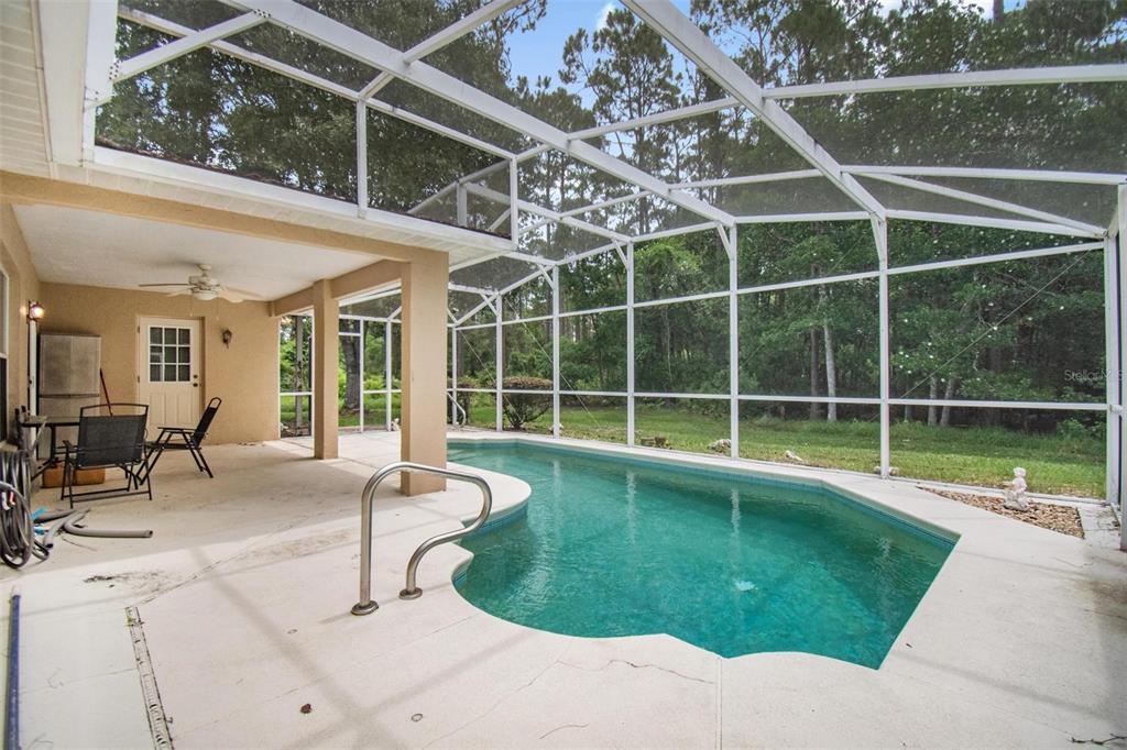 A screened-in patio features a swimming pool, concrete decking, and a view of trees — 17 EBB TIDE DRIVE, PALM COAST, FL