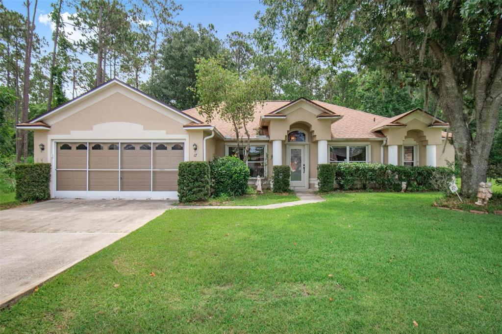 A single-story house with a tan stucco exterior, a two-car garage, and a landscaped lawn — 17 EBB TIDE DRIVE, PALM COAST, FL