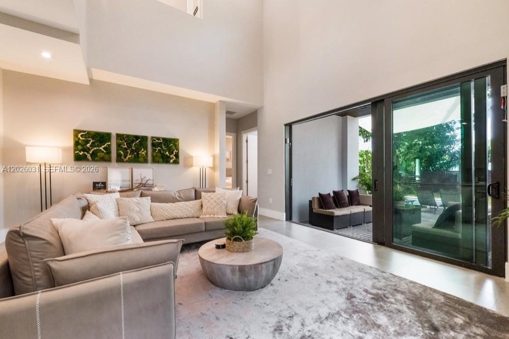 A modern living room features a sectional sofa, high ceilings, and sliding glass doors to a patio — 3379 William Ave, Miami FL 33133, MIAMI, FL