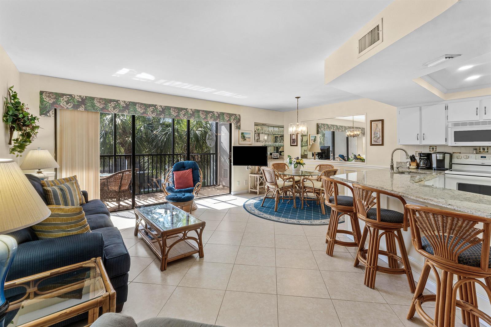 An open-concept living and dining area features tile floors, rattan furniture, and a kitchen island — 1605 S Us Highway 1 # D302, Jupiter FL 33477, JUPITER, FL
