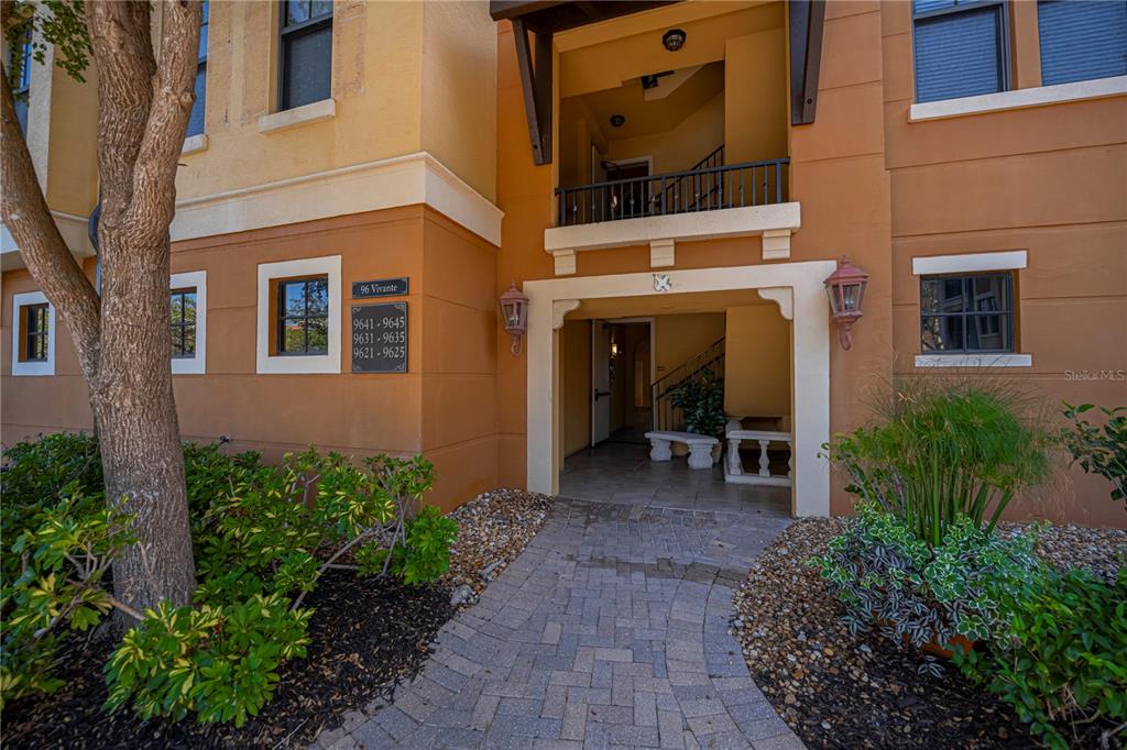 The exterior of a multi-story apartment building features a paved walkway leading to an entrance — 96 VIVANTE BOULEVARD UNIT 24, PUNTA GORDA, FL