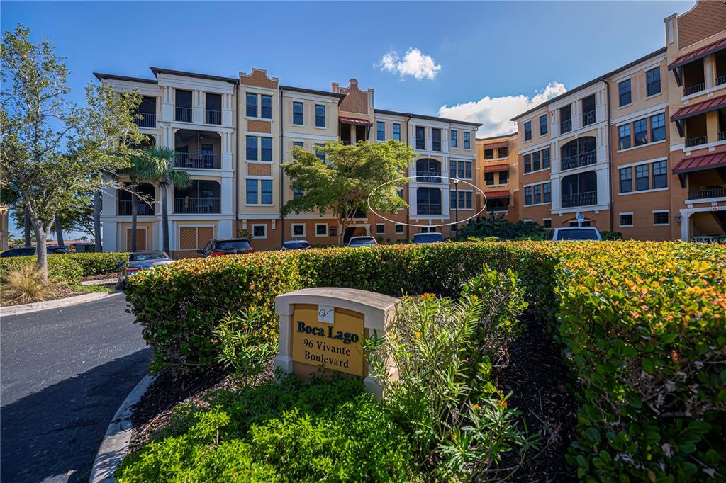A multi-story apartment building with a circled balcony is viewed behind a landscaped entrance sign — 96 VIVANTE BOULEVARD UNIT 24, PUNTA GORDA, FL