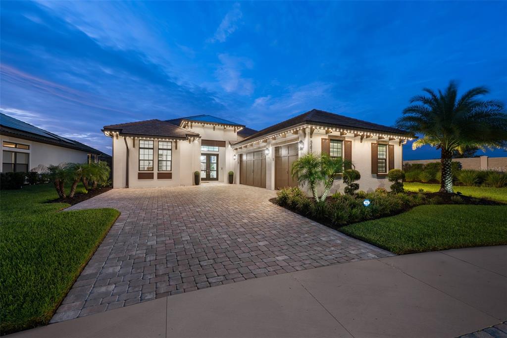 A single-story house with a paved driveway, a two-car garage, and exterior lighting at dusk — 34135 TOMPION WAY, WESLEY CHAPEL, FL